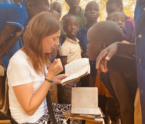 Die Bereichsleiterin Alexandra Blattnig-Rull der Auslandshilfe der Caritas Kärnten sitzt bei einem Projektbesuch umringt von Kindern der Schule und fragt diese wie es ihnen geht.