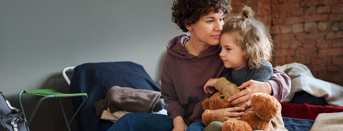 Alleinerziehende sind besonders häufig von Armut betroffen Eine Frau sitzt auf einer Bank, auf ihrem Schoß ein kleines Kind mit Kuscheltier in der Hand.